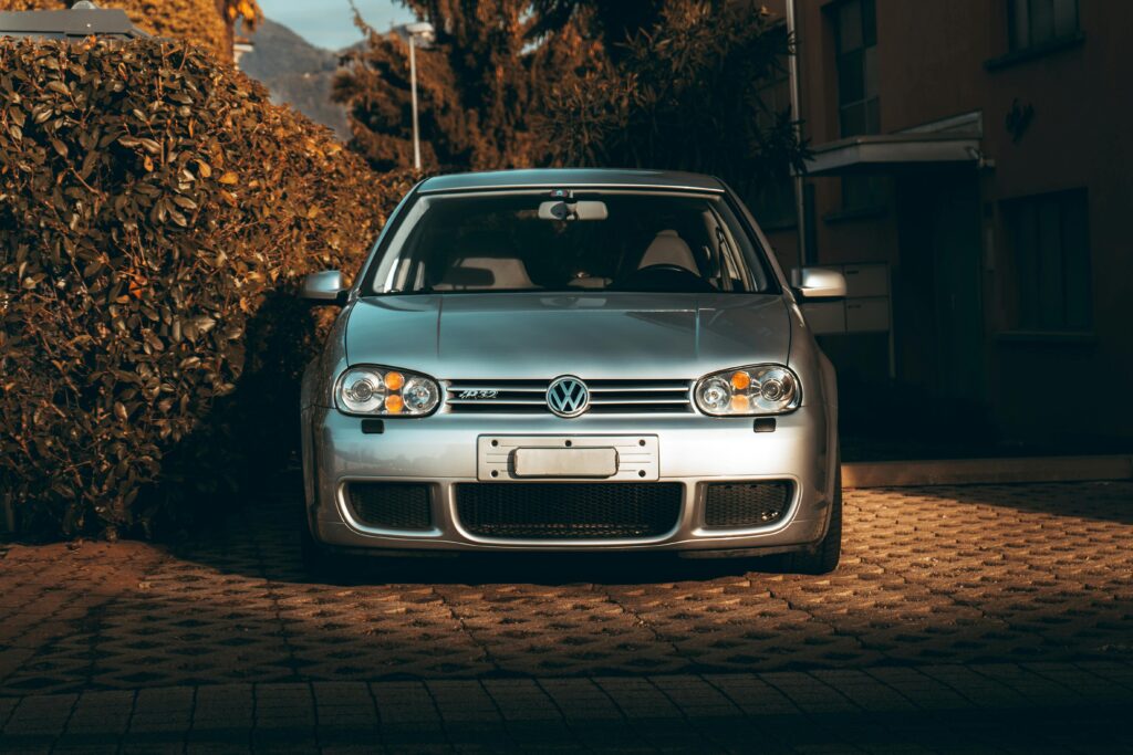 Front view of a silver Volkswagen Golf R32 parked next to a hedge in sunlight.